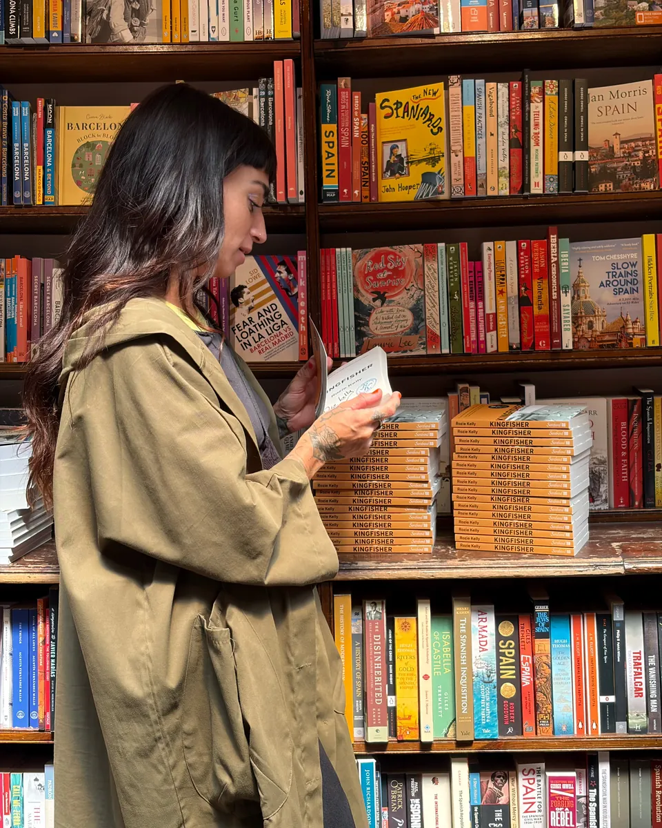 Rozie Kelly holding a copy of Kingfisher beside stacks of the book in a bookshop